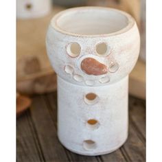 a white vase sitting on top of a wooden table with holes in it's face