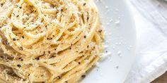 a white plate topped with pasta covered in parmesan cheese and seasoning next to a fork