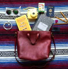 the contents of a woman's purse laid out on a striped blanket with sunglasses, books and other items