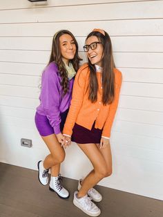 two young women standing next to each other in front of a white wall wearing purple and orange sweaters