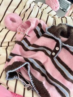 a pink and brown sweater laying on top of a bed next to a laptop computer