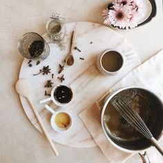 a marble plate topped with bowls filled with liquid and whisks next to flowers