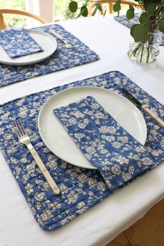 a table set with place settings and flowers in a vase on the tablecloths