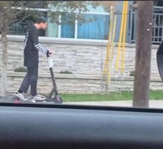 a man riding on the back of a scooter next to a car window