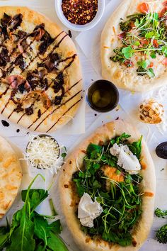 four pizzas with different toppings on them sitting on top of a white table