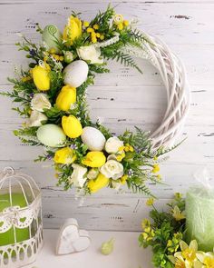 a white wreath with yellow and white flowers on it next to a birdcage