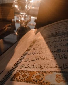 an open book sitting on top of a table next to a glass vase and candle