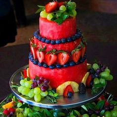 a three tiered cake with fruit on top and grapes, strawberries, blueberries, oranges, raspberries