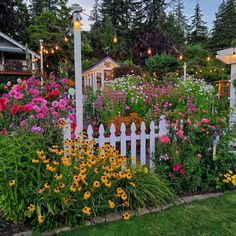 a white picket fence surrounded by lots of flowers and lights in front of some houses