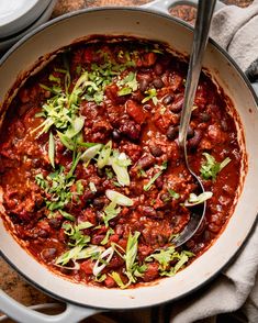 a pot filled with chili and beans on top of a wooden table next to silverware