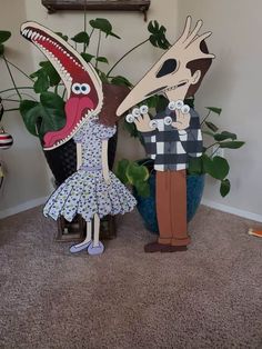 two paper cut outs of people standing in front of plants and a fake dinosaur head