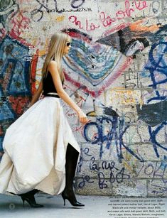 a woman in black and white dress walking past graffiti covered wall with writing on it