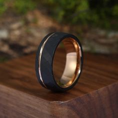 a black and gold wedding ring sitting on top of a wooden table in front of some bushes