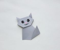 an origami cat with big eyes on it's head is shown in grey paper