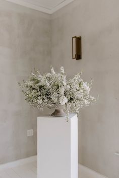 a vase filled with white flowers sitting on top of a wooden floor next to a wall