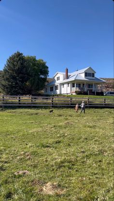 two children are playing in the grass near a fence and a large white house on a sunny day