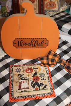 an orange pumpkin sitting on top of a black and white checkered table cloth next to a wooden sign