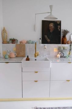 a kitchen with white cabinets and gold trim on the counter top, has a painting above the sink