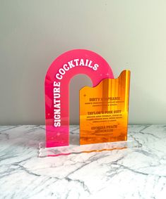 a pink and yellow sign sitting on top of a marble counter next to a white wall