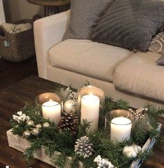 some candles are sitting on a tray with pine cones and evergreen branches in it, along with other christmas decorations