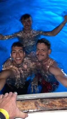 three men in a swimming pool with their arms around each other and one man smiling