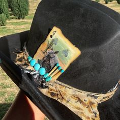 This is a unique western style hat with a custom band. The band is tan, white, black, and twine. It is embellished with turquoise stones, matches, and an armadillo playing card. Handmade Western Hat Bands For Western-themed Events, Artisan Hat Bands For Kentucky Derby Festival, Handmade Hat Bands For Kentucky Derby, Handmade Artisan Hat Bands For Western-themed Events, Handmade Western Hats For Kentucky Derby, Handmade Country Hat Bands For Western-themed Events, Handmade Southwestern Hat For Kentucky Derby, Handmade Western Costume Hats For Kentucky Derby, Artisan Fedora Hat Bands For Western-themed Events