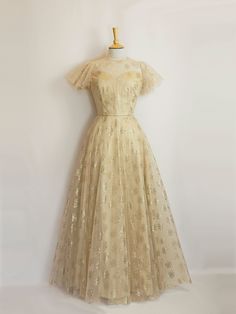 This gold silk and tulle gown would make a stunning alternative wedding dress or a decadent evening gown. The under layer is a luxurious pale gold silk dupion and the overlay is a featherlight art deco rose printed tulle. It can also be made in a shorter length for a 1950s vintage style dress.  It features a high necked version of our Bustier Grace bodice, with an illusion neckline and a keyhole opening at the back. The gently flared silhouette of the silk underlayer is then complemented by the Ethereal Gown With Sheer Bodice For Party, Ethereal Tulle Evening Dress For Party, Champagne Tulle Evening Dress, Elegant Gold Tulle Evening Dress, Gold Tulle Evening Dress For Formal Occasions, Champagne Tulle Gown For Gala, Gold Tulle Gown For Gala, Vintage Tulle Dress For Formal Occasions, Ethereal Organza Gown For Parties