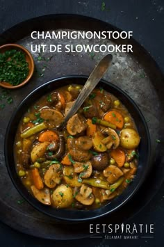 a bowl filled with stew and vegetables on top of a black plate next to a spoon