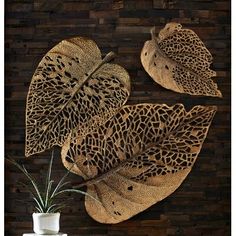 three decorative leaf shaped wall hangings in front of a wooden wall with a vase and plant