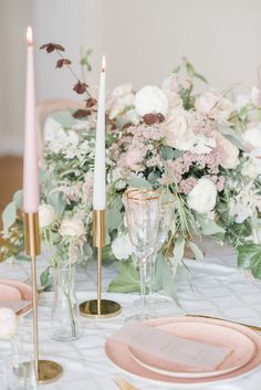 the table is set with pink and white flowers, candles, and gold chargers on it