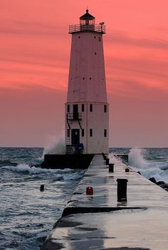 a light house sitting on top of a pier next to the ocean under a pink sky