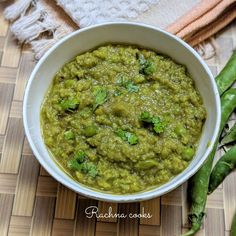 a white bowl filled with green food on top of a wooden table next to a towel