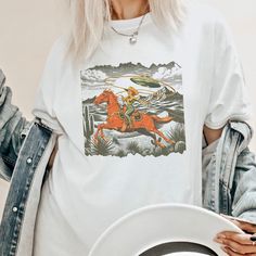 Get ready to show your style with our Retro Cowgirl Lasso T-Shirt! Perfect for a beach party, concert or or just a casual day out, this graphic tee is a must-have.  Proudly Printed on Comfort Colors® tees, for that insanely soft, vintage look and feel.  Without doubt, this will be your favorite shirt. With its vintage-inspired design, this shirt is perfect for those who love a boho, western, or retro look. The oversized fit and soft, comfortable fabric make it the perfect choice for a day on the Unisex Custom Print Shirt For Summer, Summer Pop Culture Crew Neck Shirt, Fun Short Sleeve T-shirt For Music Festival, Unisex Tops For Summer Music Festival, Summer Graphic Print Unisex Shirt, Short Sleeve Shirt With Graphic Print For Music Festival, Graphic Tee Shirt For Summer Music Festival, Summer Graphic Tee Shirt For Music Festival, Unisex Custom Print T-shirt For Summer