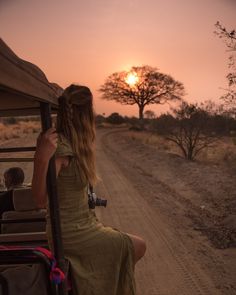 a woman sitting in the back of a truck on top of a dirt road next to trees