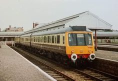 a yellow and white train traveling down tracks next to a loading platform at a train station