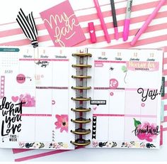 an open planner book with pink and black accessories on it, next to some pens