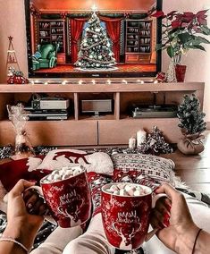 two people sitting on a couch holding red mugs in front of a christmas tree