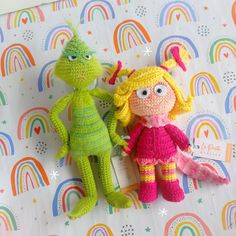 two crocheted dolls sitting on top of a rainbow - themed sheet with the word happy written on it