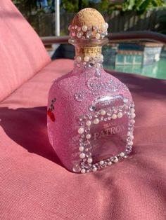 a bottle that is sitting on top of a pink bed sheet with beads and pearls around it