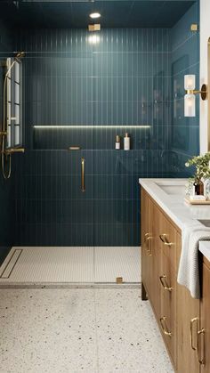 a bathroom with blue tile and gold fixtures on the shower wall, along with two sinks