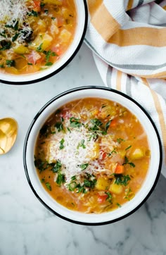 two bowls of vegetable soup with parmesan cheese on top and spoons next to it