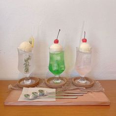 three different types of ice cream on a wooden tray with spoons and utensils