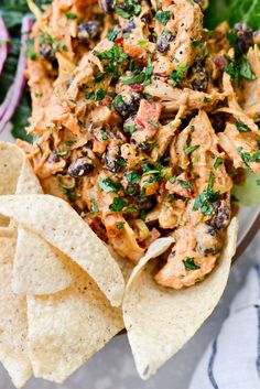 a white plate topped with tortilla chips and chicken salad next to a green leafy salad