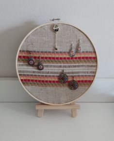 an embroidery hoop with earrings hanging from it's sides on a wooden stand next to a white wall