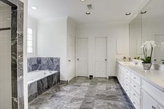 a large bathroom with marble floors and white walls, along with two sinks on either side of the bathtub