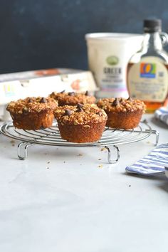 several muffins on a wire rack next to a bottle of maple syrup and other ingredients