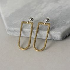 These modern earrings combine mixed metals and clean contemporary lines. They feature small 4mm sterling silver teardrop studs paired with raw brass ovals. The silver studs have a bright polished shine while the brass has a hammered texture. The ovals are 30mm long and about 14mm wide and have a warm golden color that contrasts nicely with the silver. The earrings are lightweight and comfortable and the brass shapes dangle beneath the posts for subtle movement. The total length of the earrings f Minimalist Brass Earrings For Everyday, Modern Hammered Earrings For Everyday, Modern Everyday Brass Earrings, Modern Brass Earrings For Everyday, Minimalist Silver Linear Earrings In Brass, Minimalist Hammered Bronze Earrings, Minimalist Brass Drop Earrings, Modern Rectangular Brass Earrings, Nickel Free Bronze Minimalist Earrings