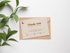 a thank you card sitting on top of a piece of paper next to a plant