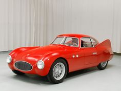 an old red sports car is parked in front of a white curtained wall and floor