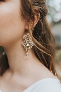 a close up of a woman's face wearing large gold and crystal earring